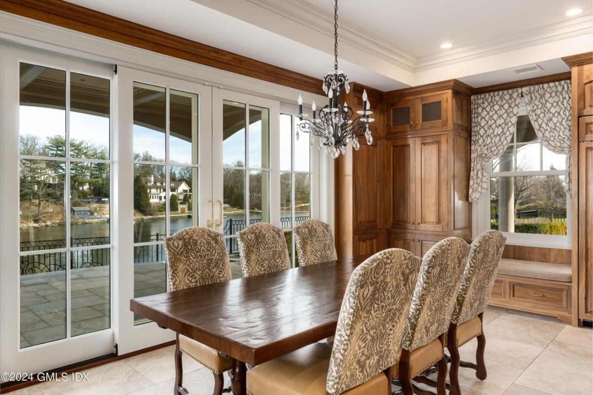 A dining room with windows, a chandelier, white ceiling, and a dining table surrounded by chairs.