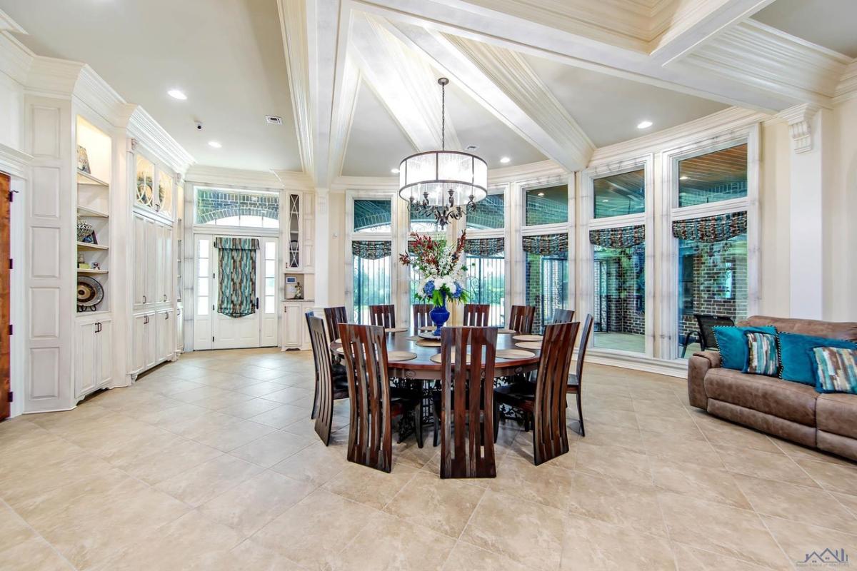 Dining room with a wooden table, chairs, chandelier and glass windows.