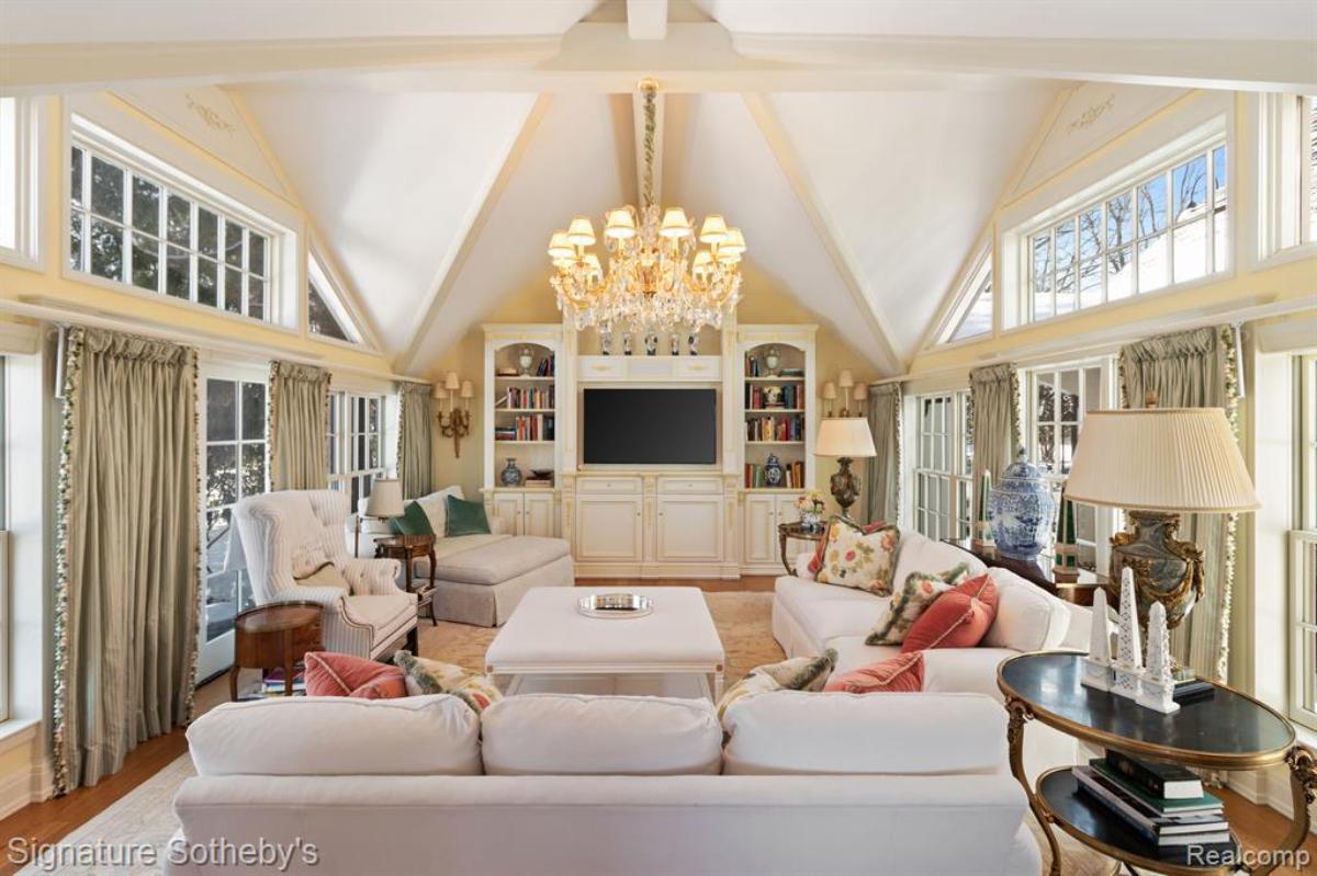 Living room with couches, TV, glass windows and a chandelier.
