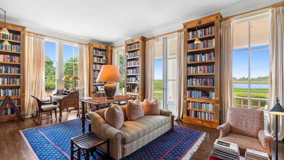 Library with wooden shelves, couch, large rug and glass doors.