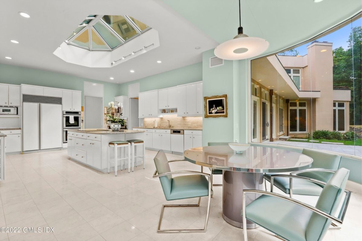A kitchen with a tiled floor, countertop, white cabinets, breakfast nook, and a white ceiling with glass features.
