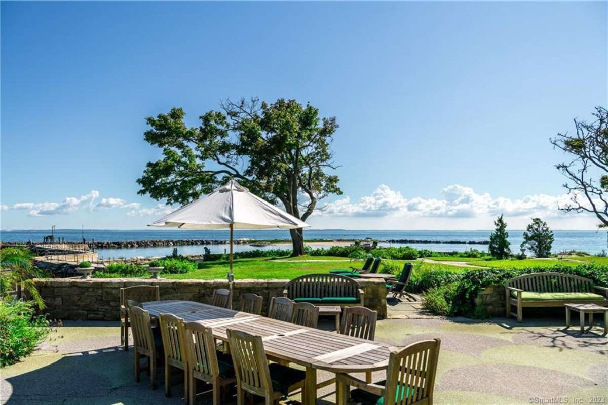 A patio with a long table surrounded by chairs, benches, tables, and an umbrella.