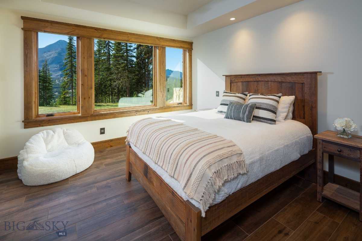 A bedroom with a bed, wooden floor, side table, and windows.