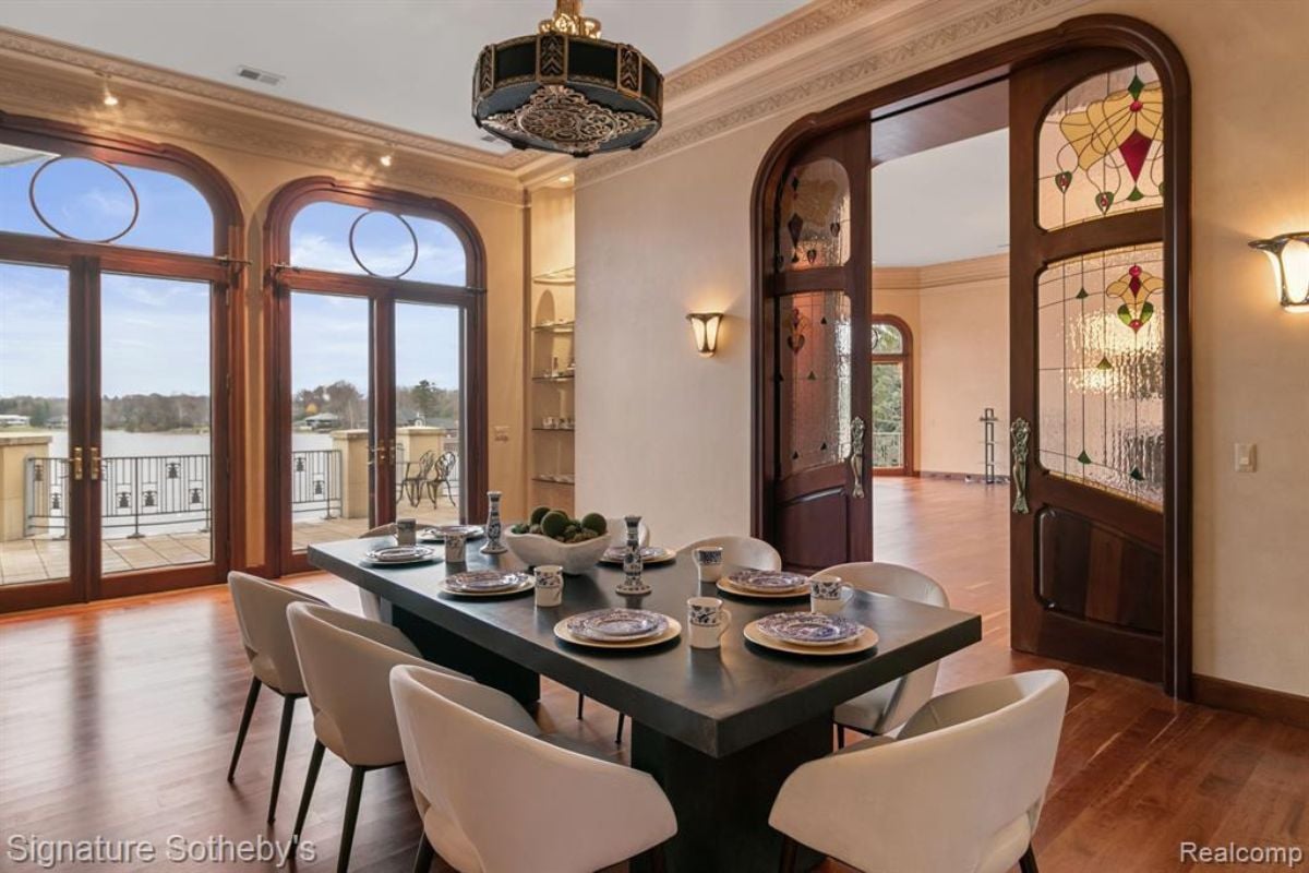 A dining room with a wooden floor, a chandelier, a wooden dining table surrounded by chairs.