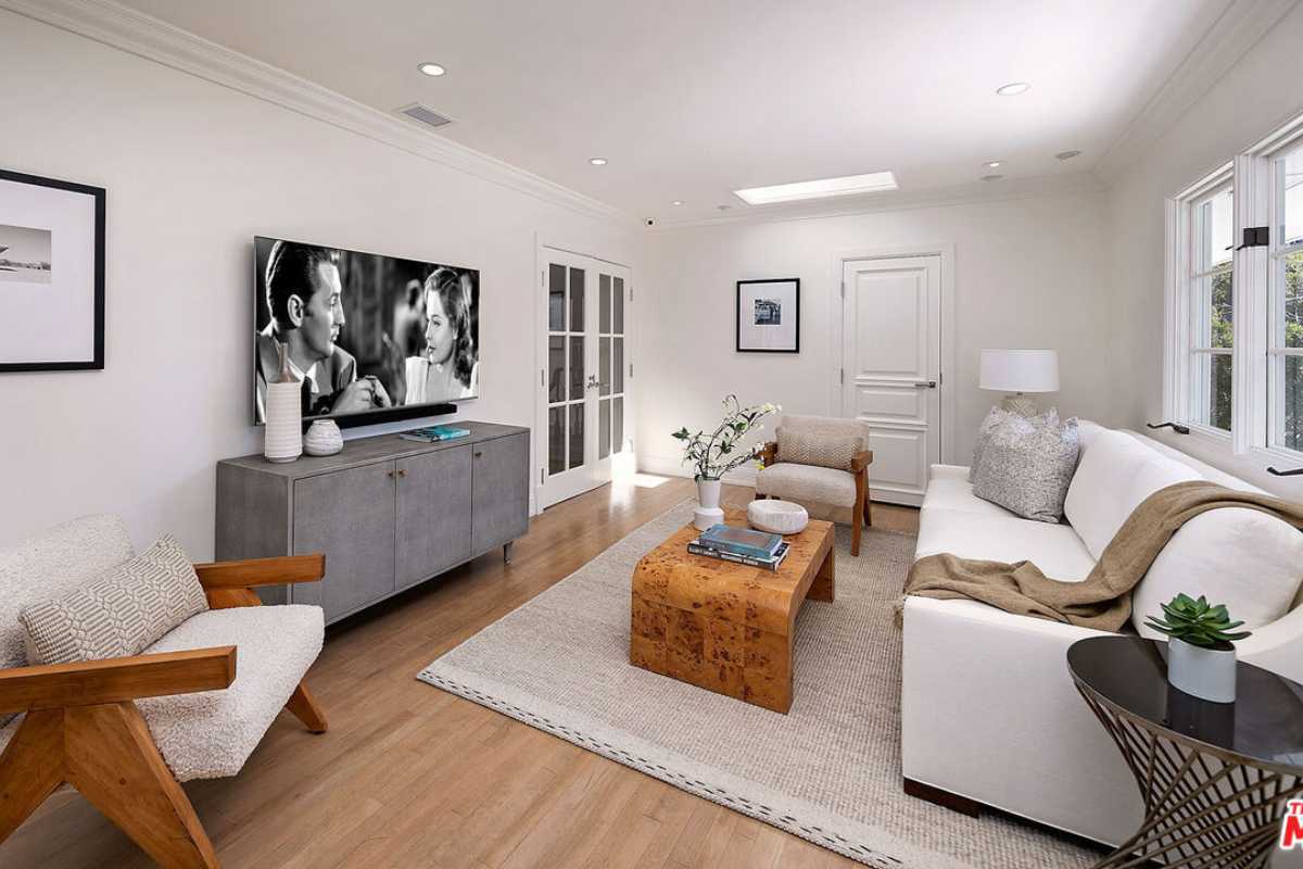 A living room with a wooden floor, rug, white ceiling, windows, TV, cabinet, couches, and a coffee table.