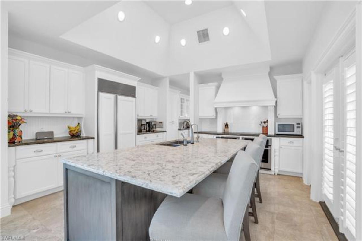 Kitchen with a large island, stove, white custom cabinets and custom lights.