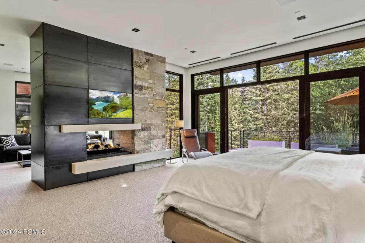 Bedroom with a large bed, TV, fireplace, carpet flooring and glass doors.