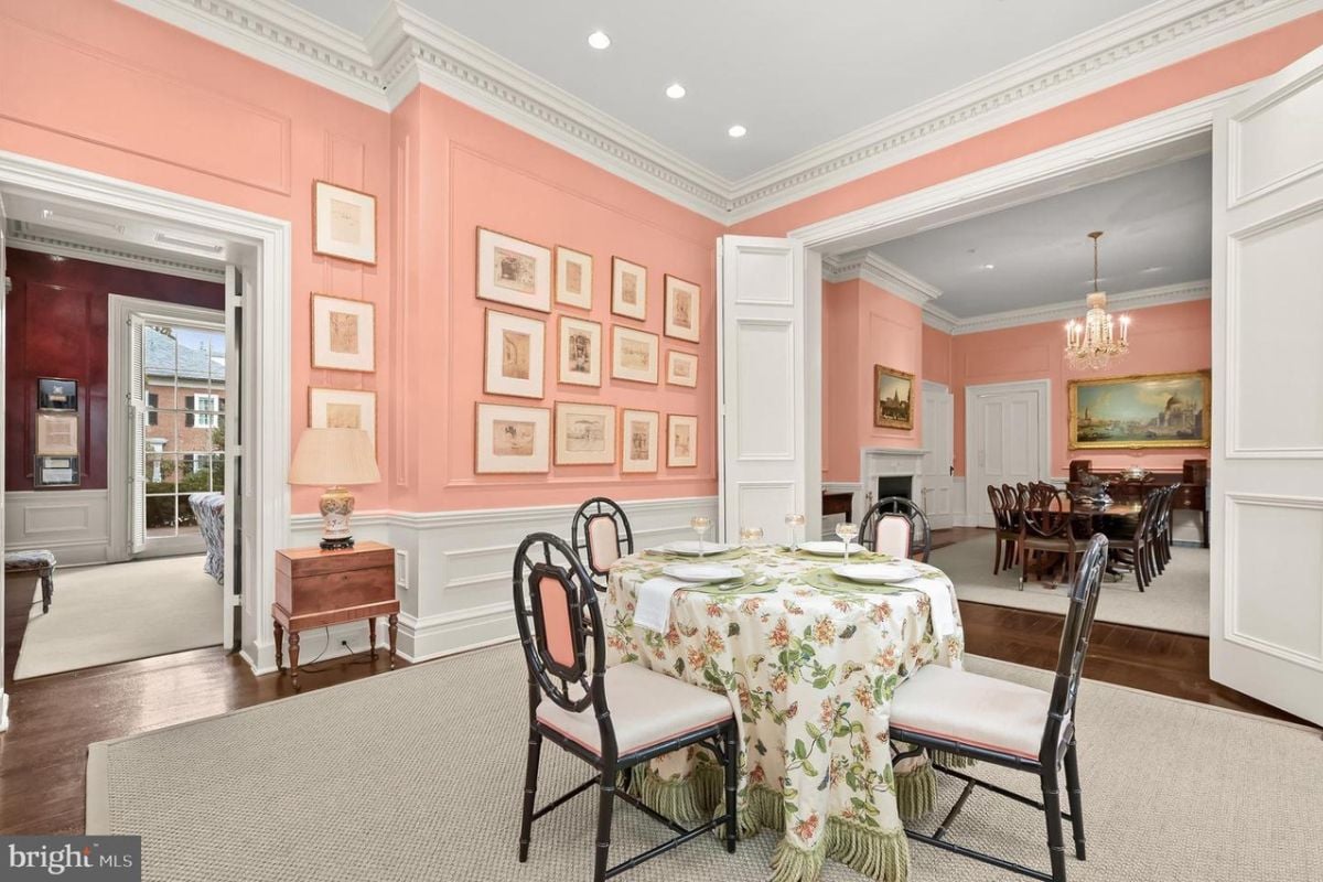 A breakfast nook with pink walls, white ceiling, wooden floor, rug, and a table surrounded by chairs.