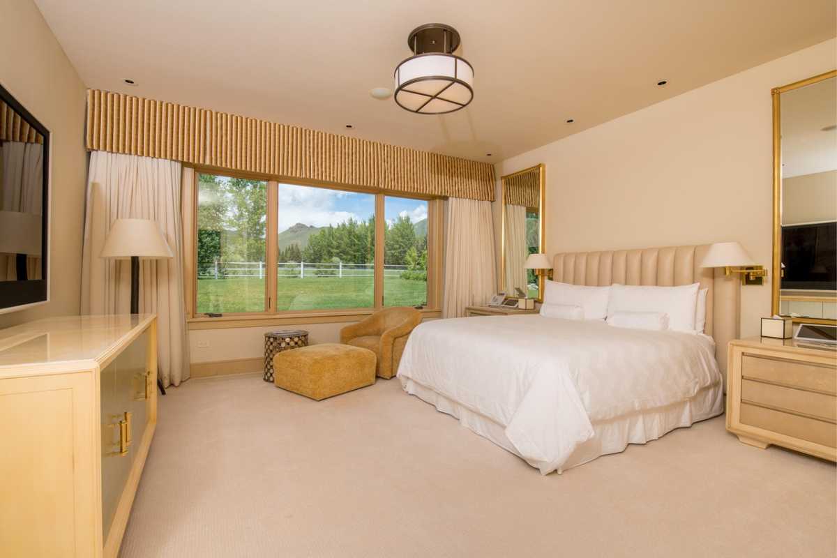 A bedroom with a bed, TV, cabinet, nightstand, couch, windows, mirrors, and a white ceiling.