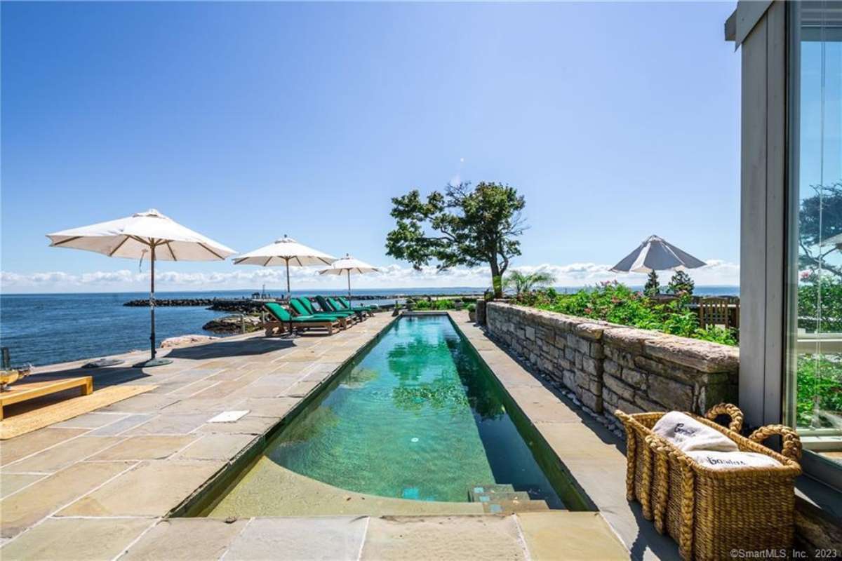 A narrow swimming pool with chairs and an umbrella.