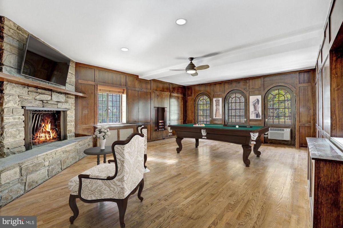 A game room with a wooden floor, a white ceiling, a fireplace TV, a ceiling fan, and a pool table.