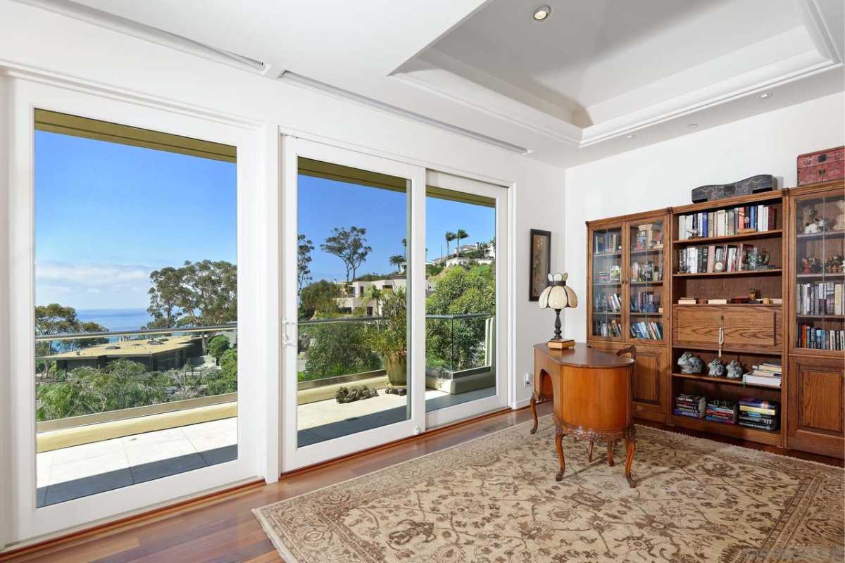 A home office with a wooden floor, rug, white ceiling, shelves, cabinets, desk, and chair.