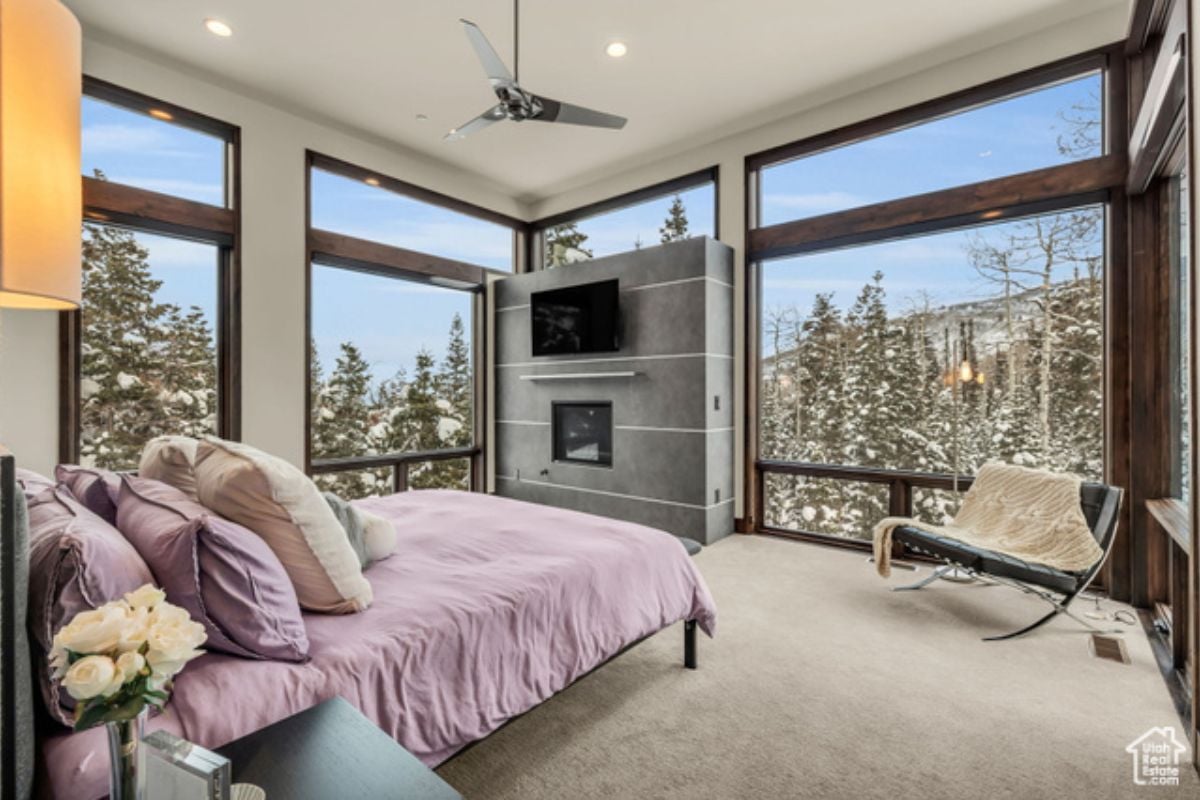 A bedroom with a bed, TV, windows, ceiling fan, and white ceiling.