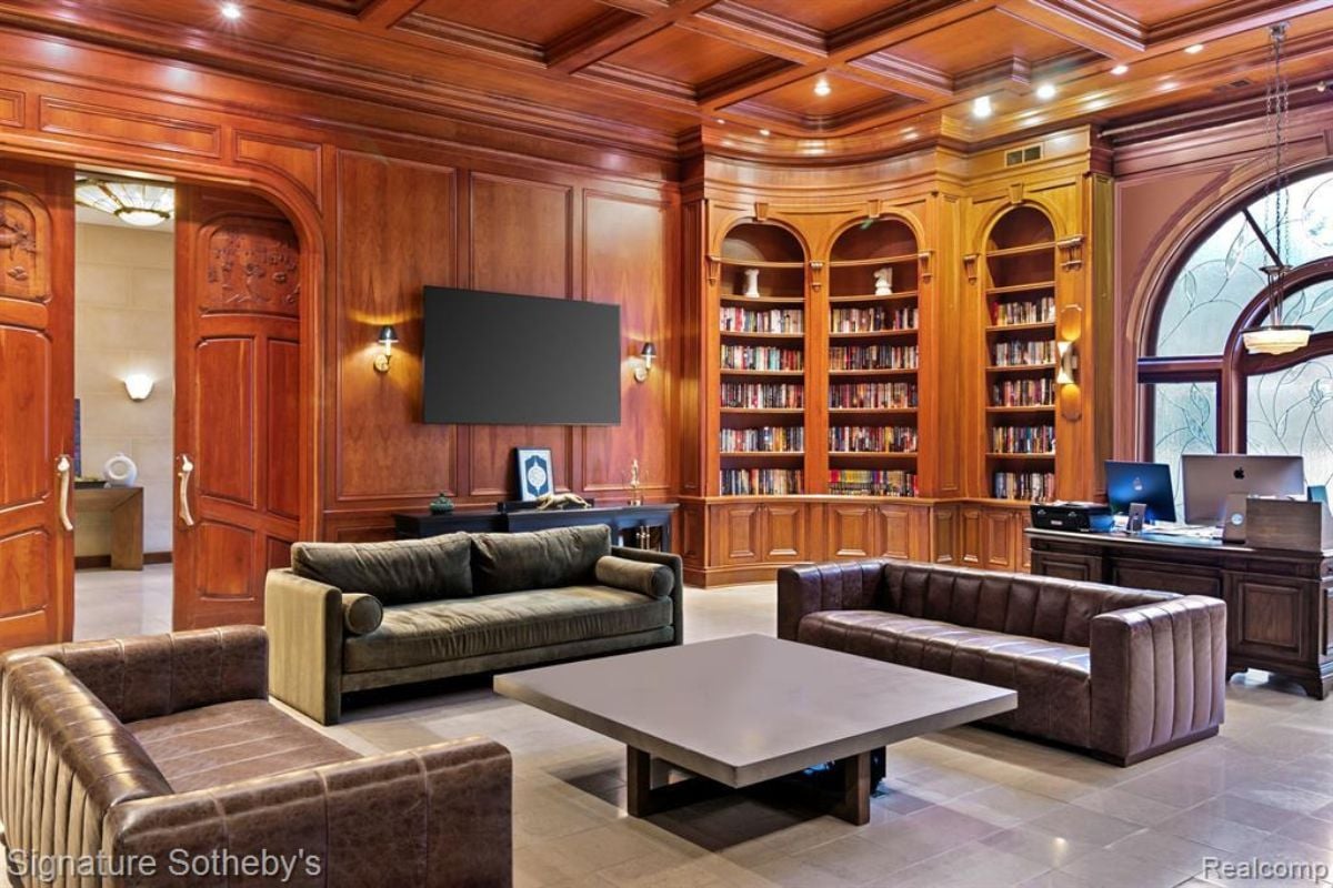 A home office with couches, a center table, a TV, shelves, a desk, and chairs.