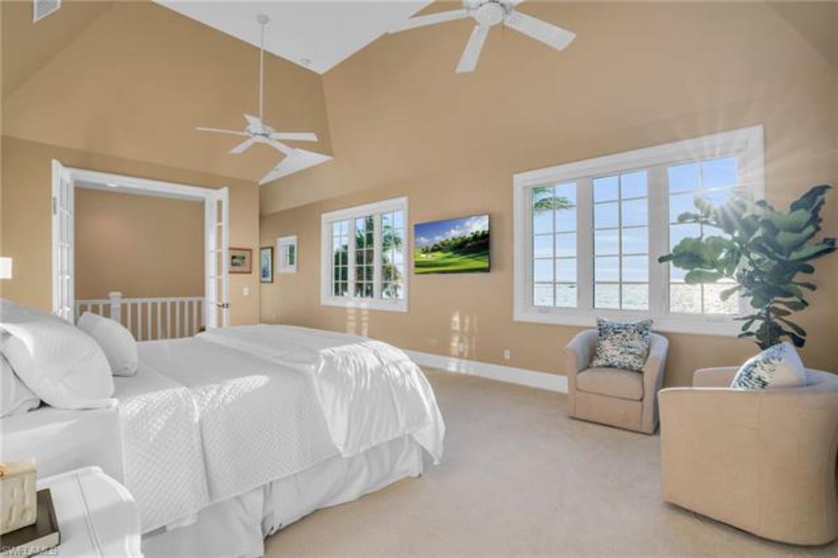 Bedroom with a large bed, carpet flooring, ceiling fans and glass windows.