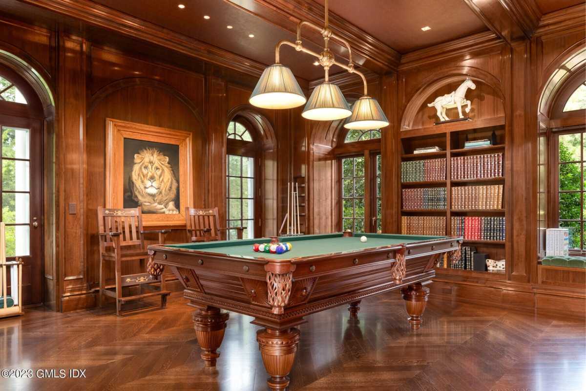 A game room with hardwood floors, a shelf, beamed ceiling, windows, painting, and a pool table.
