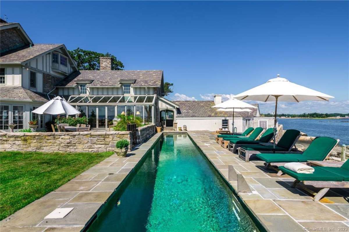 A narrow swimming pool with chairs and an umbrella.