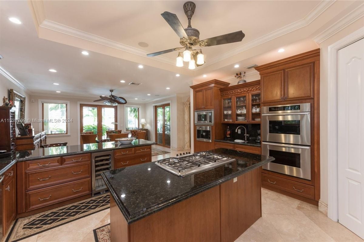 A kitchen with an island, wooden cabinets, a sink, tiled floor, a white ceiling, and a ceiling fan.