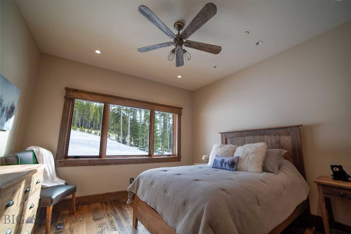 A bedroom with a bed, wooden floor, side table, cabinet, chair, ceiling fan, and windows.