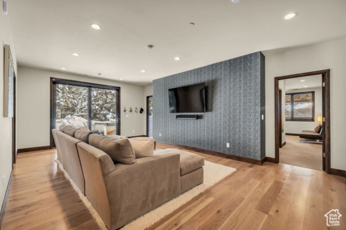 A lounge with wooden floor, couch, white ceiling, window, and TV.
