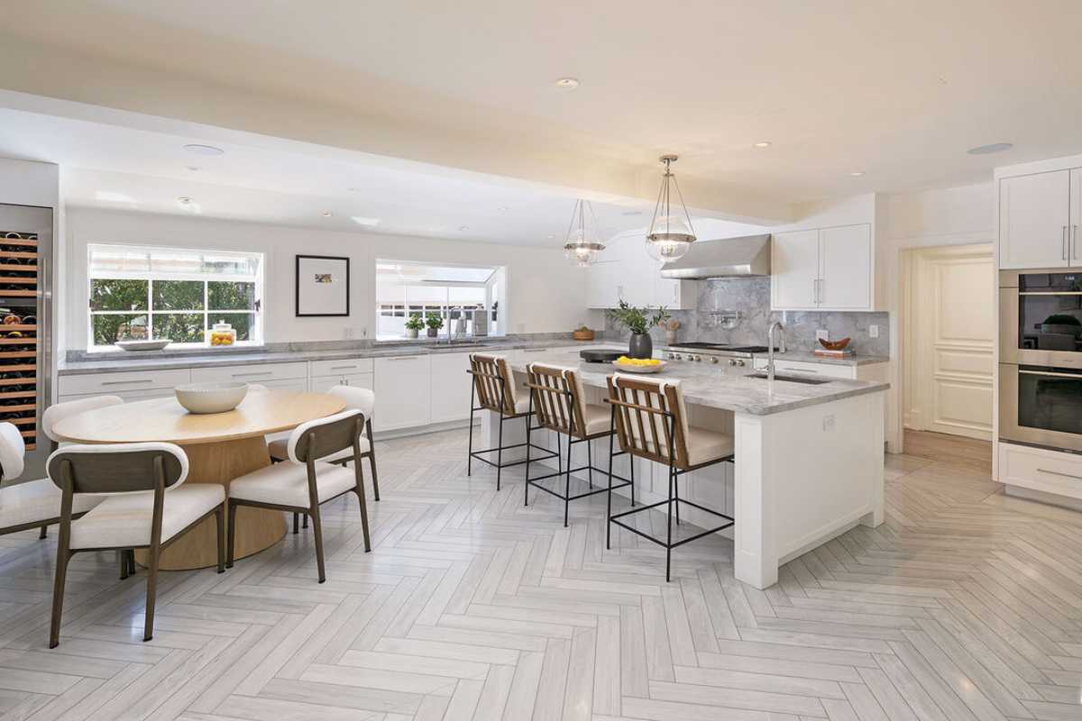 A kitchen with countertops, chairs, a white ceiling, windows, kitchen appliances, and a dining table.