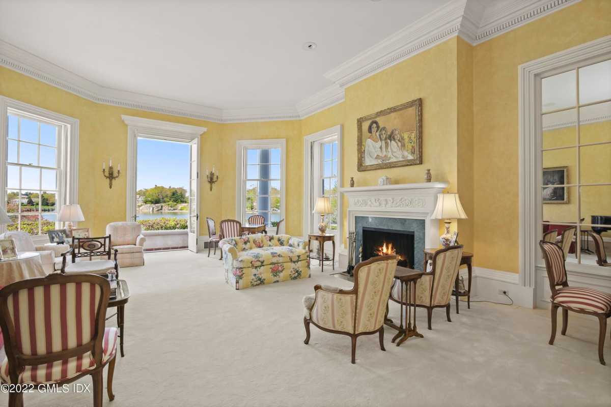A living room with a fireplace, yellow walls, windows, a white ceiling, couches, and chairs.