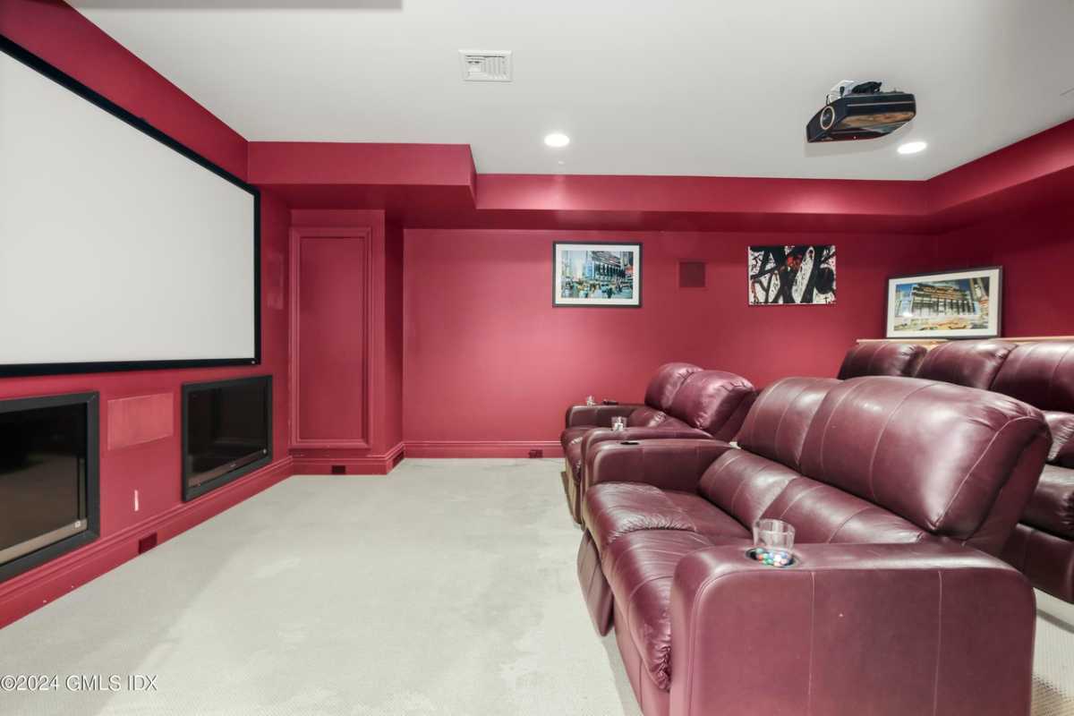 A home theater with red couches, red walls adorned with paintings, a large screen, and a white ceiling.