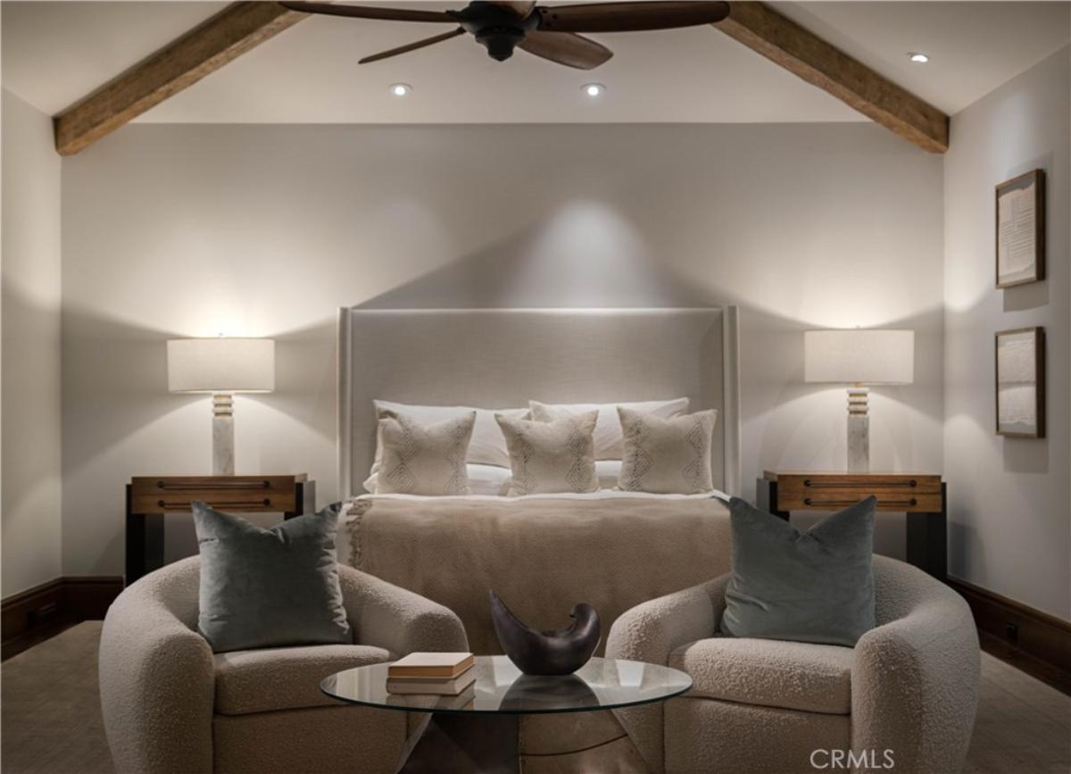 Bedroom with a large bed, sitting area, ceiling fan and a carpet flooring.