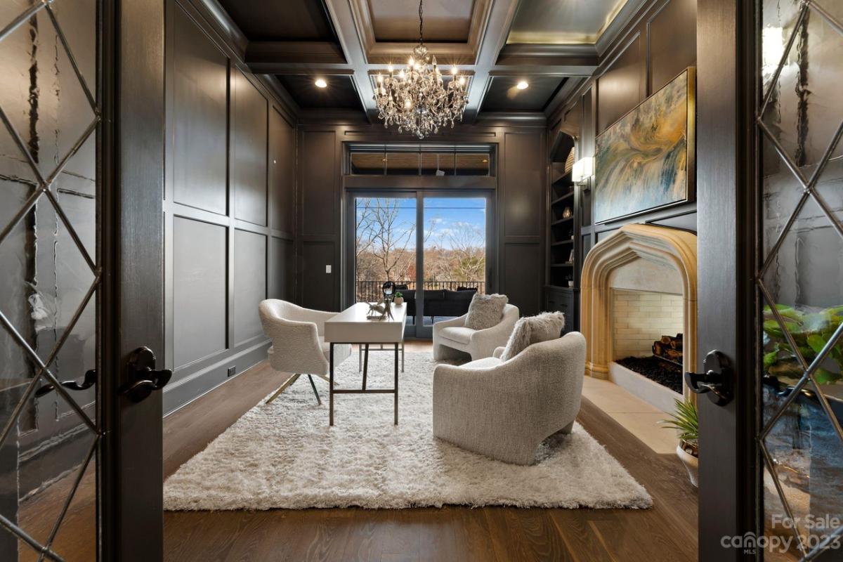 Home office with a desk, large rug, chandelier and a wood flooring.