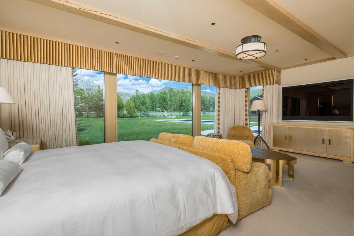 A bedroom with a bed, TV, cabinet, nightstand, couch, windows, and a white ceiling.