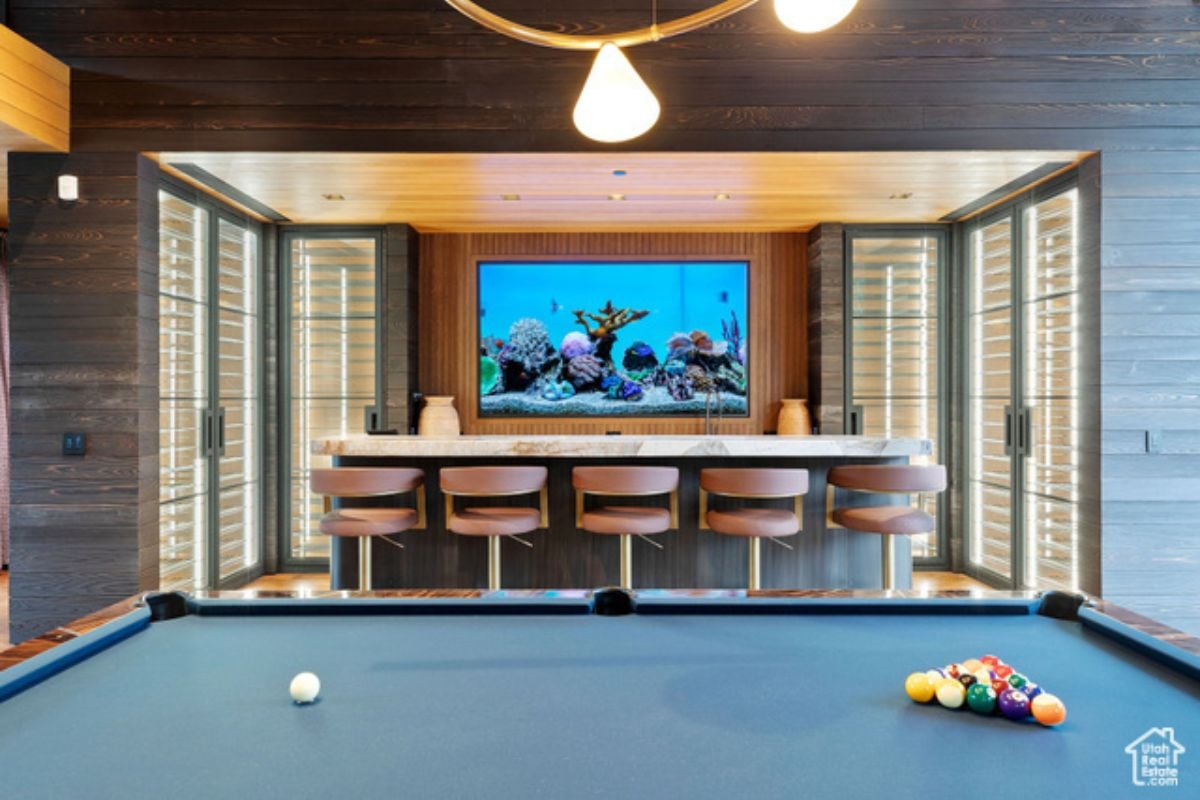 A bar with a counter, chairs, TV, and pool table.