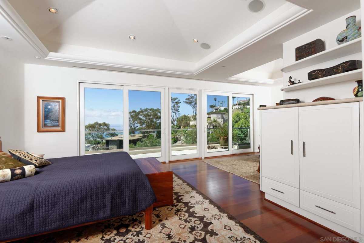 A bedroom with hardwood floors, a bed, rug, white cabinet, and a white ceiling.
