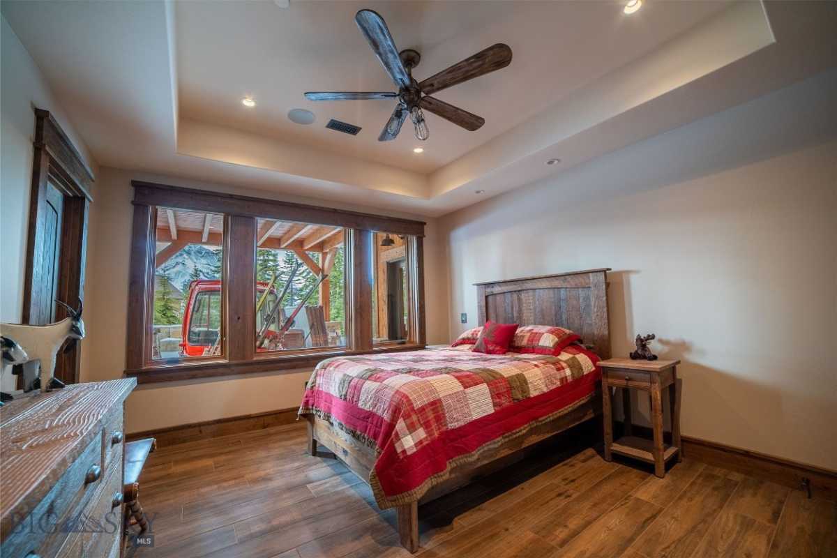 A bedroom with a bed, wooden floor, side table, cabinet, ceiling fan, and windows.