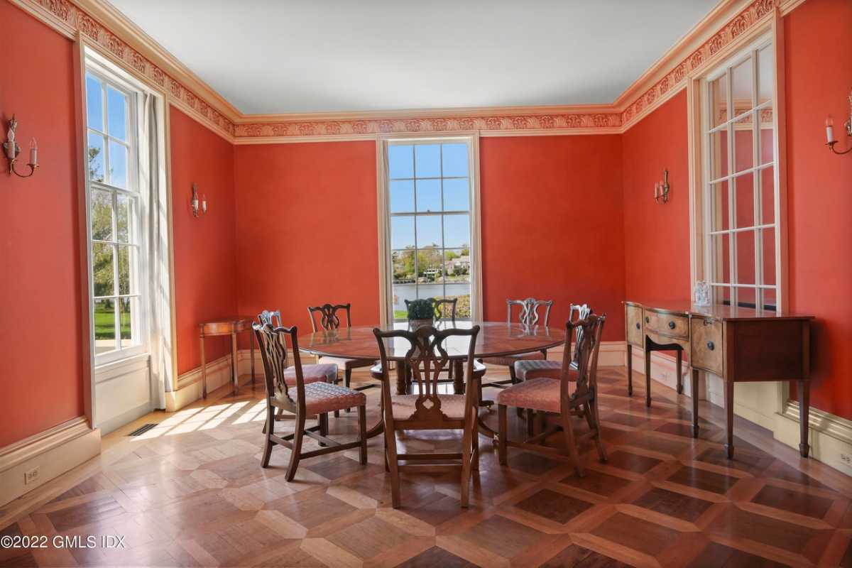 A dining room with a tiled floor, orange walls, windows, a white ceiling, a cabinet, and a dining table surrounded by chairs.