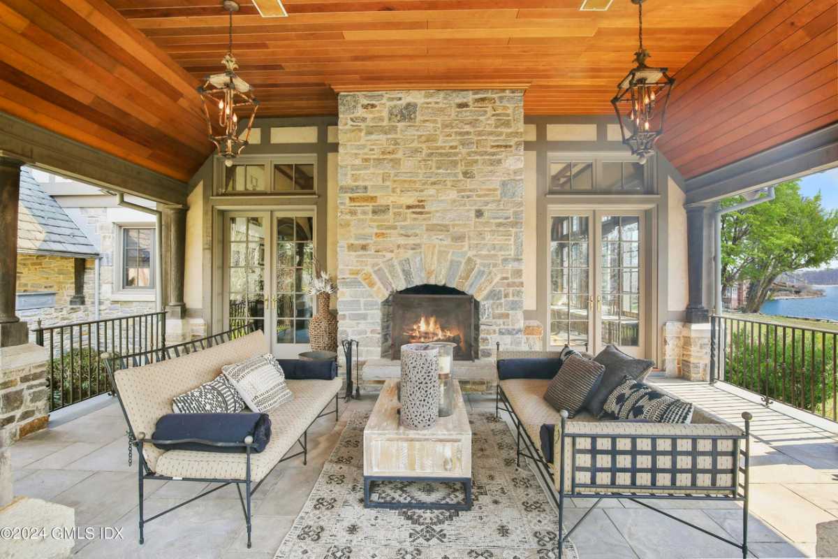 A porch with a stone fireplace, a wooden ceiling, a rug, couches, and a coffee table.