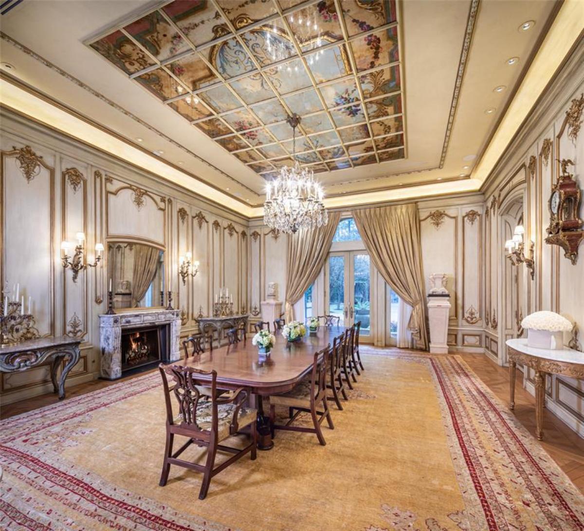 Dining room with a large table, chairs, chandelier, large rug and a fireplace.
