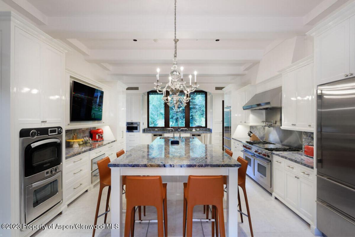 Kitchen with a large island, chandelier, chairs and a refrigerator.