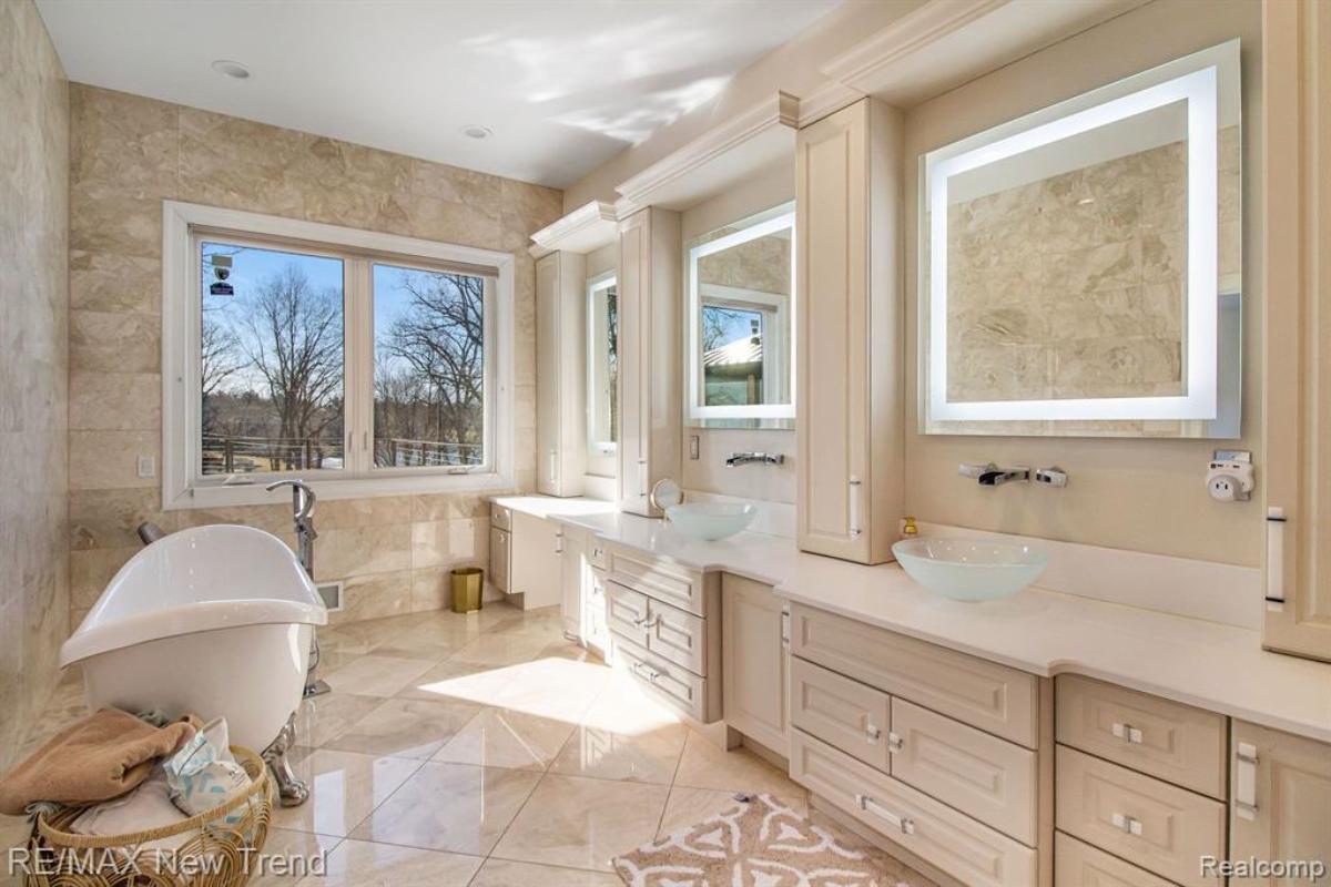 Bathroom with dual sinks, mirrors, soaking tub and tile flooring.