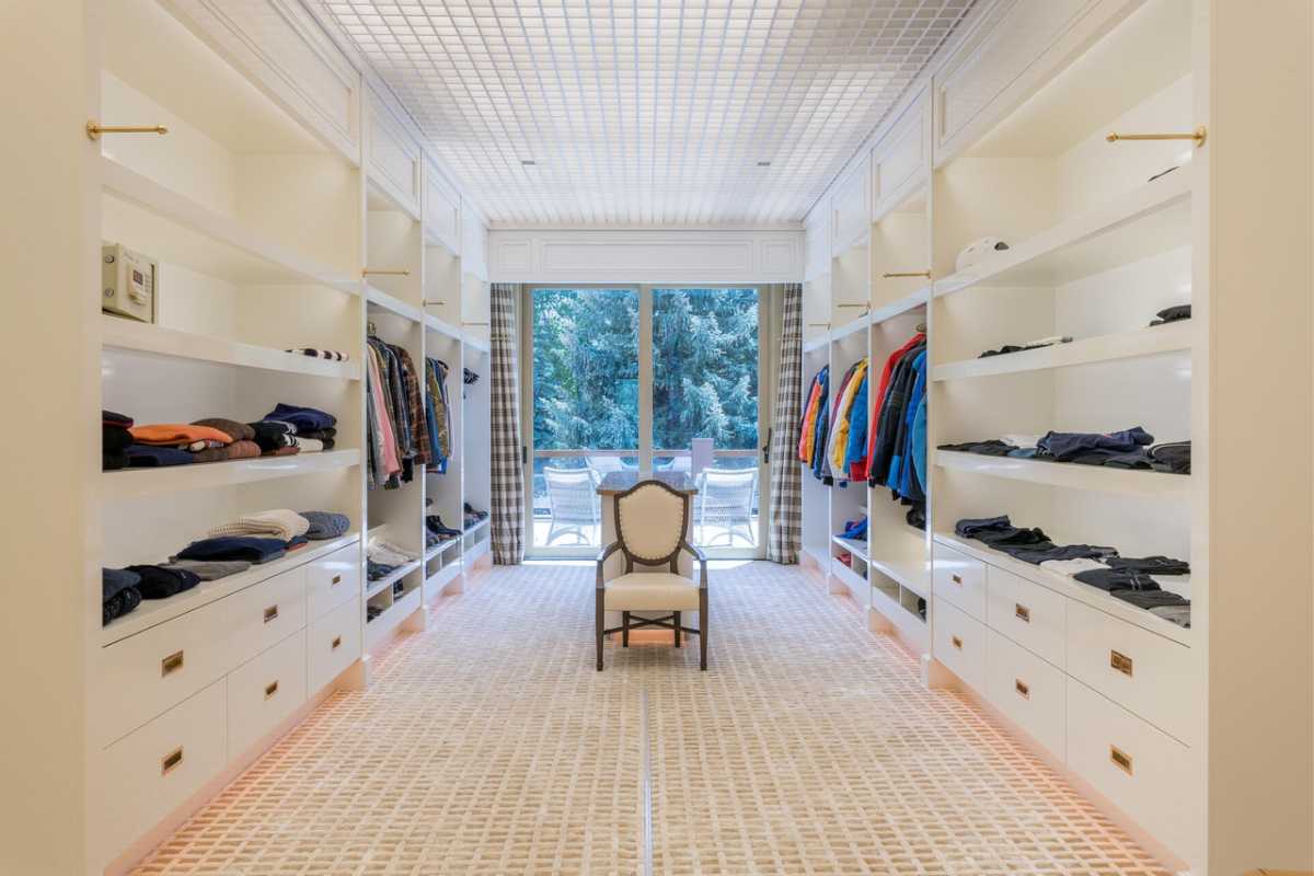 A walk-in closet with a center island, chair, white cabinets, and a white ceiling with a screen.