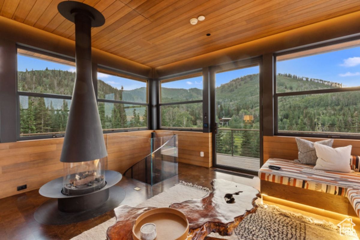 A lounge with a fireplace, wooden floor, wooden ceiling, couch, center table, and windows.