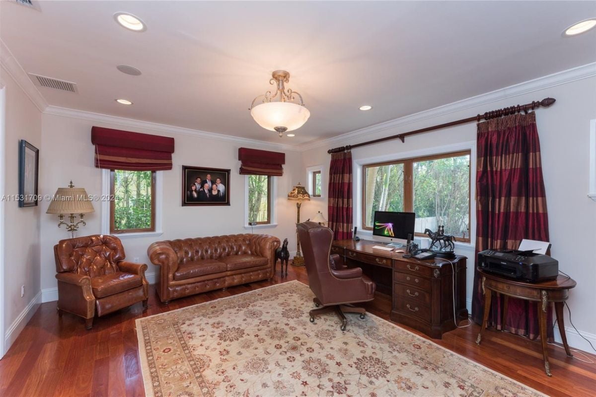 A home office with wooden floors, white walls, a white ceiling, leather couches, a chair, and a desk.