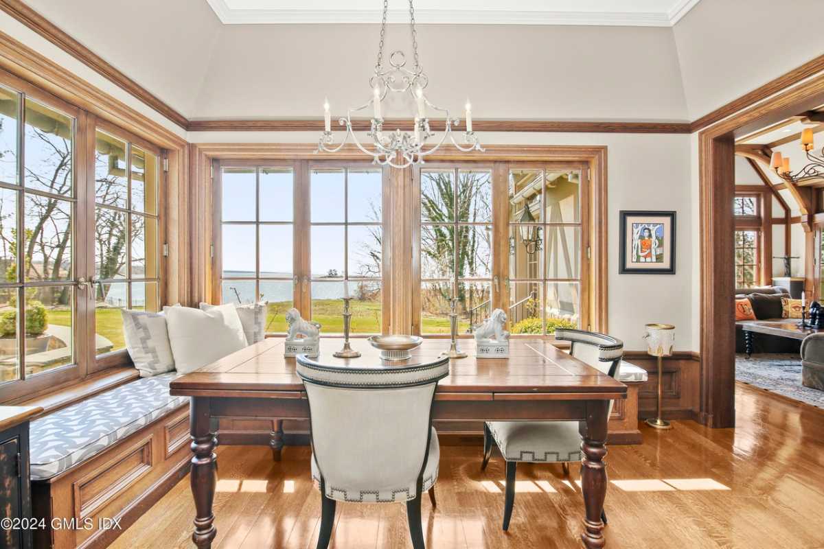 A home office with a wooden floor, a bench, a chandelier, a wooden desk, and a chair.