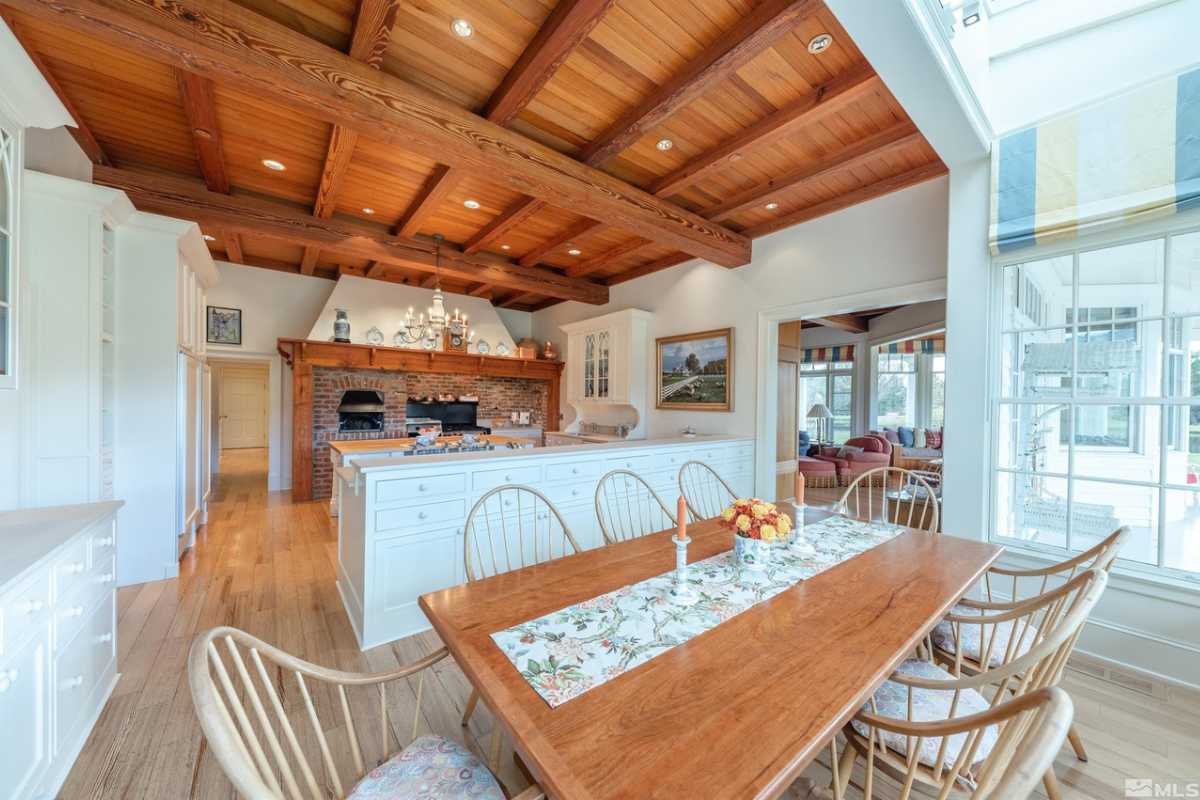 A kitchen with a wooden floor, exposed beam ceiling, countertop, oven, and a table surrounded by chairs.