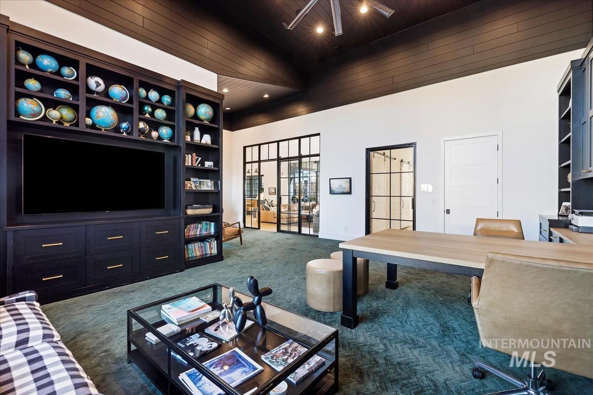 Home office with a desk, chairs, TV and a carpet flooring.