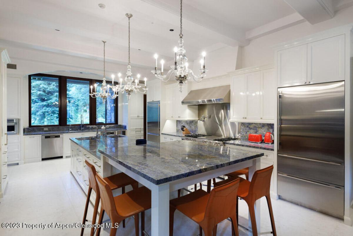 Kitchen with a large island, chandelier, chairs and a refrigerator.
