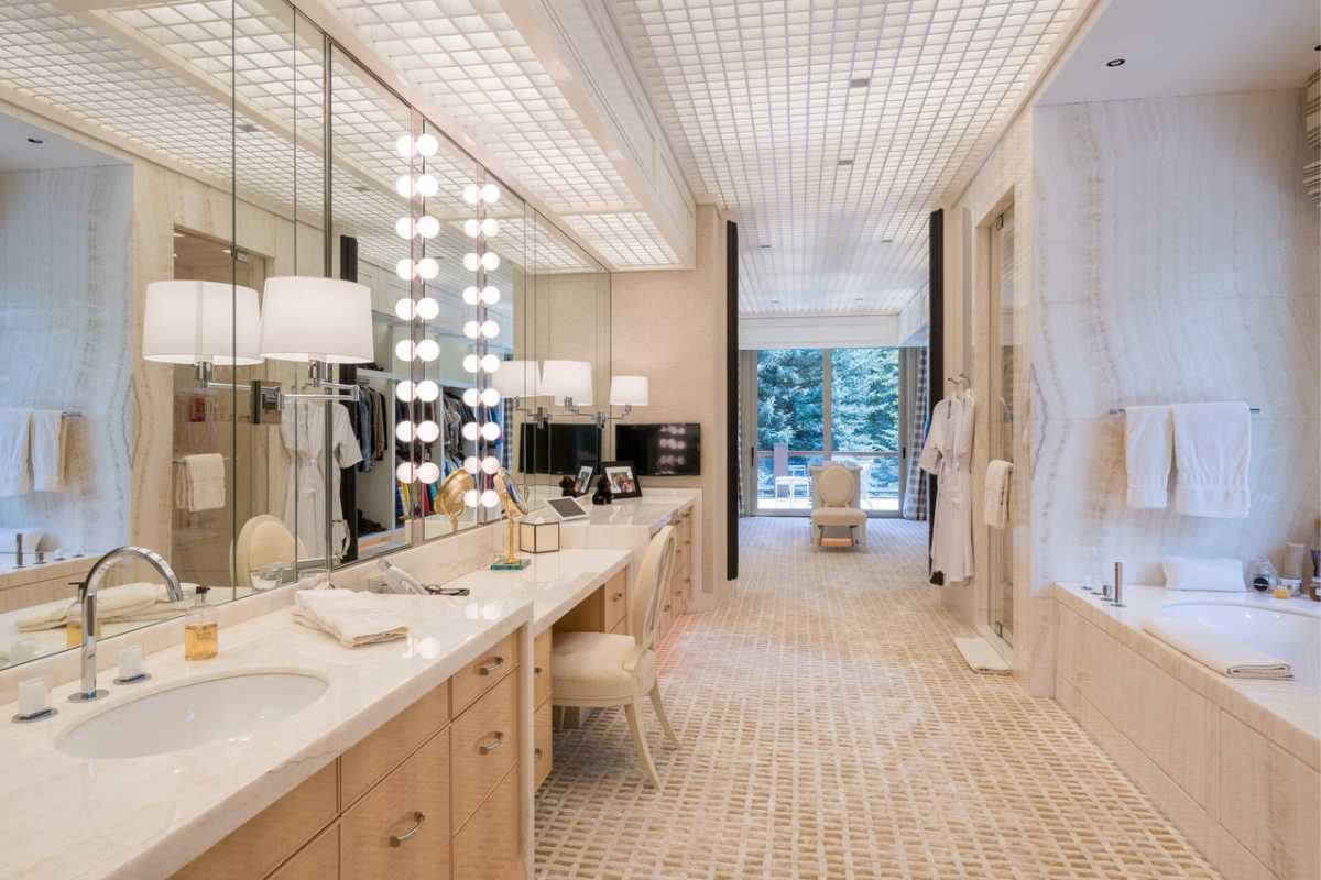 A bathroom featuring a large mirror, bathtub, sink, cabinets, countertop, and tiled floor.