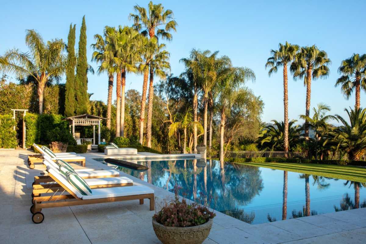 A swimming pool with trees, chairs, and a poolside.