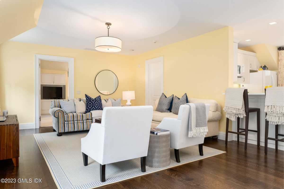 A lounge with a wooden floor, rug, couches with pillows, and chairs.