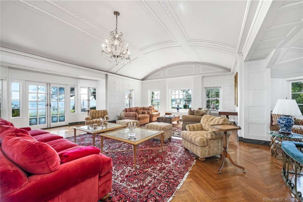 A living room with a rug, red and brown couches, a white arched ceiling, a chandelier, a coffee table, and windows.