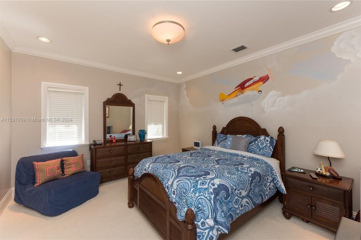 A bedroom with a bed, couch, window, white ceiling, painted walls, a nightstand, and a lampshade.